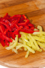 Red and green paprika sliced into strips on the wooden cutting b