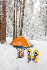 Snowshoes left in front of orange tent in winter forest