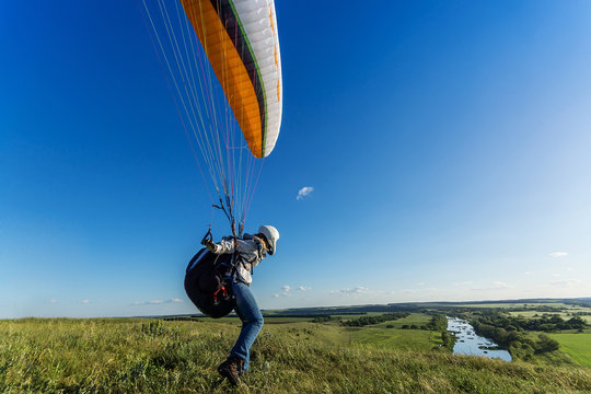 Paraglider is ready to take off over a green hill