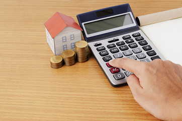 Hand on calculator with coins stack and paper house for mortgage
