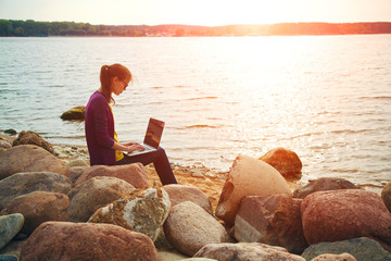 pretty girl using laptop at sunny sea stone coast