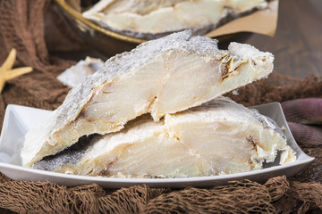 Lomos de bacalao salado cortados, pescado seco conservado en sal sobre fondo de redes de pesca