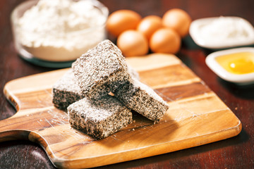 Group of Lamingtons on a timber cutting board with food ingredients in the background 