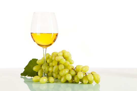 Weißwein im Glas umgeben von grünen Weintrauben