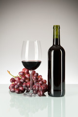 Rotwein im Glas und in der Flasche mit roten Weintrauben