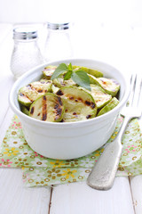 Grilled zucchini in a white plate with a fork decorated with basil