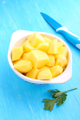 raw peeled potatoes in a white bowl on a blue background