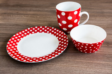 Red polka dotted plate, mug and bowl on brown table