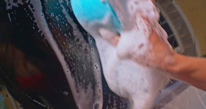 Pretty girl in bikini washing car window with foam sponge and reflecting in it 