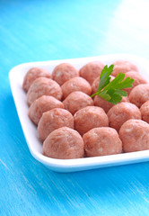 meat balls from raw minced meat in a white tray on a blue background