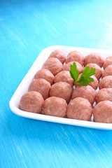 meat balls from raw minced meat in a white tray on a blue background