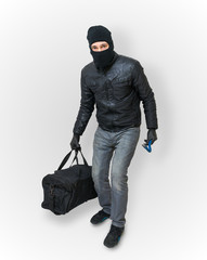Masked burglar or thief with balaclava is sneaking with black ba