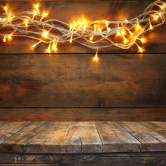 wood board table in front of Christmas warm gold garland lights on wooden rustic background....