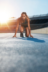 Young female sprinter in start position on racetrack - obrazy, fototapety, plakaty