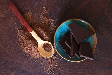 close up of  a wooden spoon, chocolate and cocoa powder on woode