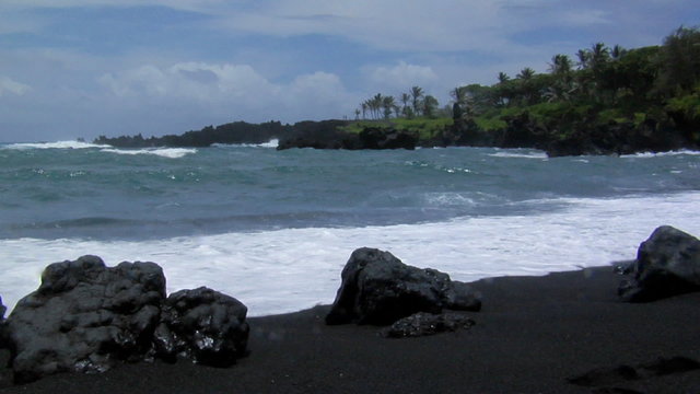 Large waves roll into a black sand beach.