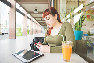 Portrait of young woman using smartphone and digital tablet while sitting in bar