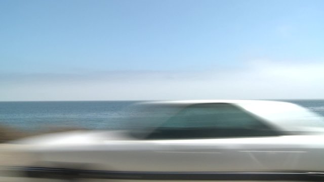 A car travels along Pacific Coast Highway as seen through the side window.