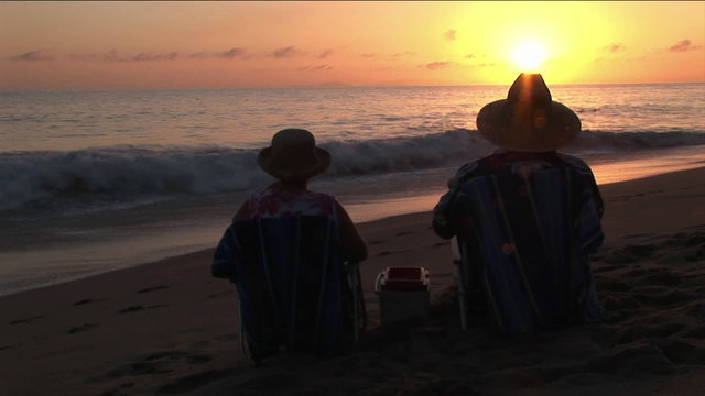 A couple toasts the ocean from their beach chairs.