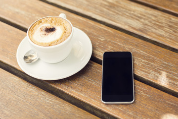 Blank cell phone and cup of coffee on a wooden table