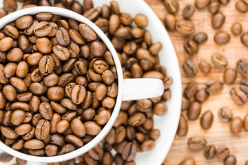 coffee beans inside white half visible cup and plate on wood background
