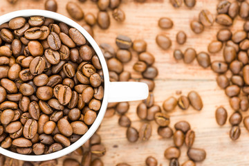 coffee beans inside white half visible cup without plate on isolated wood background
