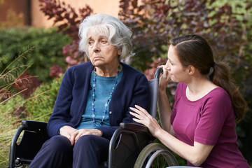 Fototapeta na wymiar Adult Daughter Comforting Senior Mother In Wheelchair