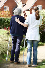 Carer Helping Senior Woman To Walk In Garden Using Walking Frame
