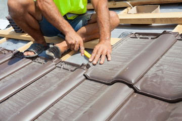 Hands of roofer laying tile on the roof. Installing natural red tile.