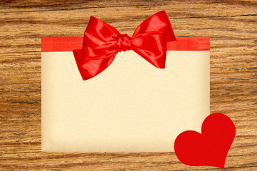 Card decorated with red ribbon, bow and heart on wooden backgrou