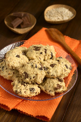 Homemade oatmeal and chocolate cookies on plate with ingredients in the back, photographed with natural light (Selective Focus, Focus on the front of the cookies)