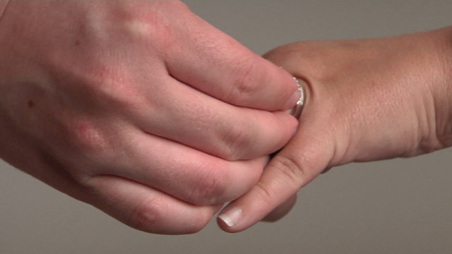 A man puts a gemstone ring on a woman's hand.