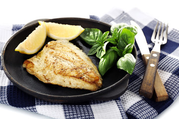 Dish of fish fillet with basil and lemon on table close up
