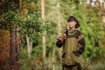 Young beautiful woman hunter with a shotgun in the forest