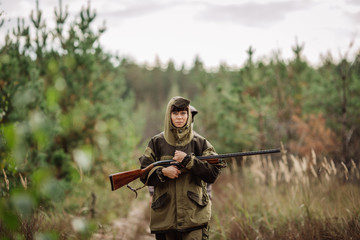 Fototapeta premium Young beautiful woman hunter with a shotgun in the forest