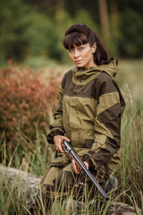 Young beautiful woman hunter with a shotgun in the forest
