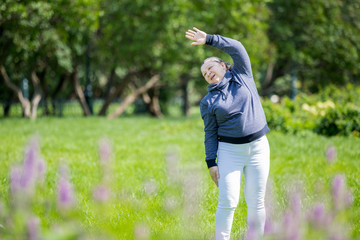 Senior woman doing exercises in green beautiful park. Healthy lifestyle