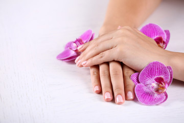Fototapeta premium Woman hands with french manicure and orchid flowers on wooden table close-up