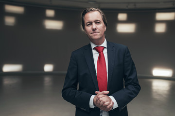 Satisfied young businessman with red tie in empty room.