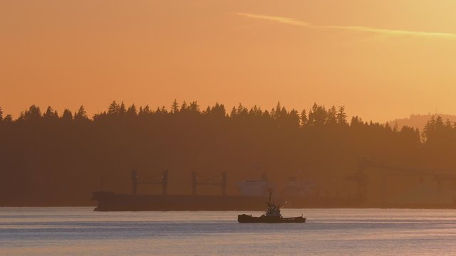 Long Cargo Boat And Small Tug In The Bay
