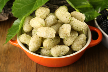 Ripe mulberries in bowls with green leaves on table close up