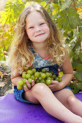 Blonde child girl with grapes in autumn vineyard