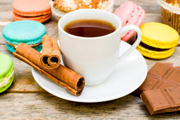 macaroon with tea, chocolate and cinnamon sticks on a wooden tab