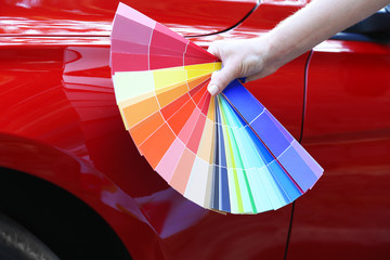 Female hand with color samples over red car background