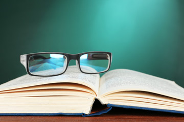 Open book with glasses on desk on green chalkboard background