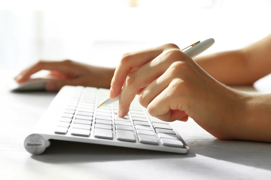 Female hand with pen typing on keyboard at table, closeup