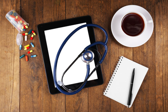 Doctor workplace with blank tablet and stethoscope on wooden background
