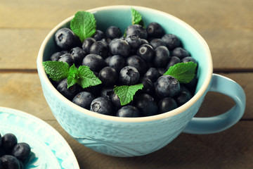 Cup and plate with fresh blueberries on wooden table close up