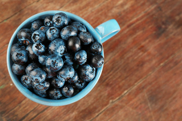 Fresh blueberries in cup on wooden table close up