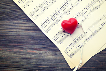 Earphones with red heart and music notes on wooden background